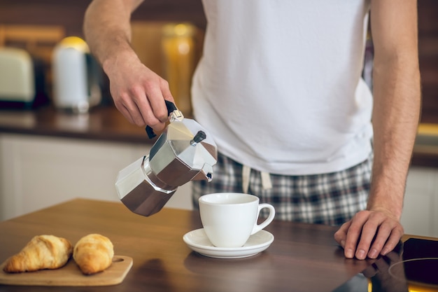 Morning coffee. Close up of man in homewear pouring coffee to the cup