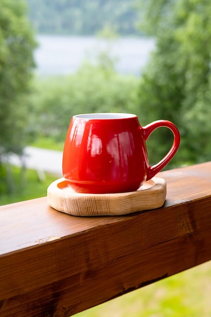 Morning coffee in garden Red mug on wooden board against blurred nature