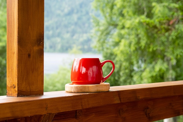 Morning coffee in garden Red mug on wooden board against blurred nature