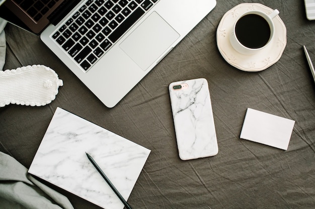 Morning coffee, laptop, marble diary, glasses in bed with grey sheet and pillows