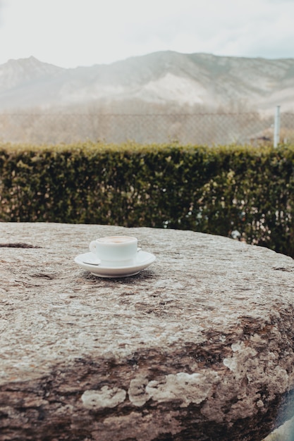 Morning cup of coffee on a old stone table with mountain background at sunrise