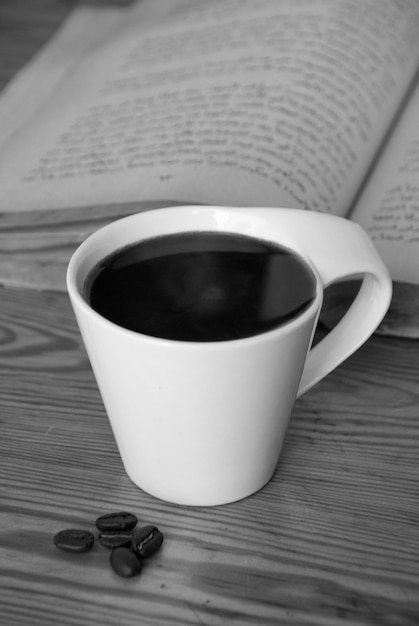 Morning cup of coffee next to roasted coffee beans and open book.