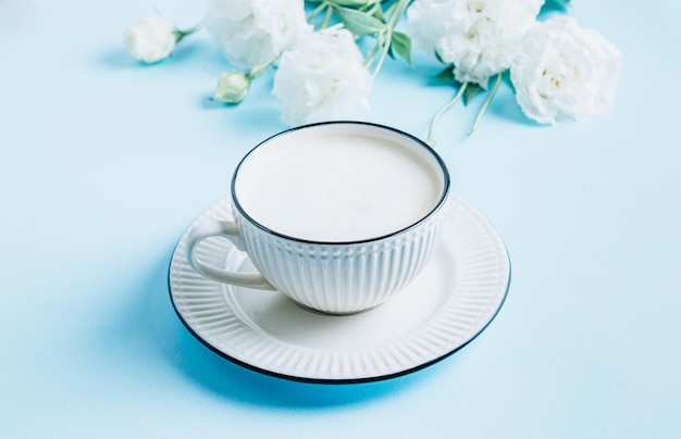 Morning cup of coffee and white eustoma flowers on blue pastel background