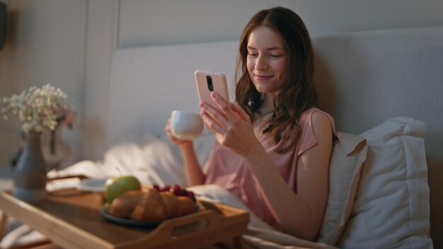 Morning female taking sip of coffee in bed closeup smiling calm girl browsing