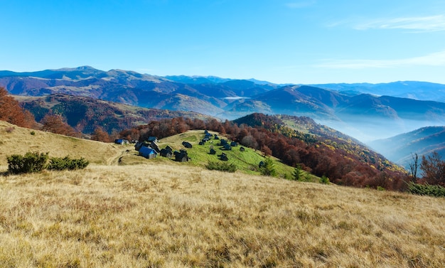 Morning fog in autumn Carpathian and wooden barns on slope.