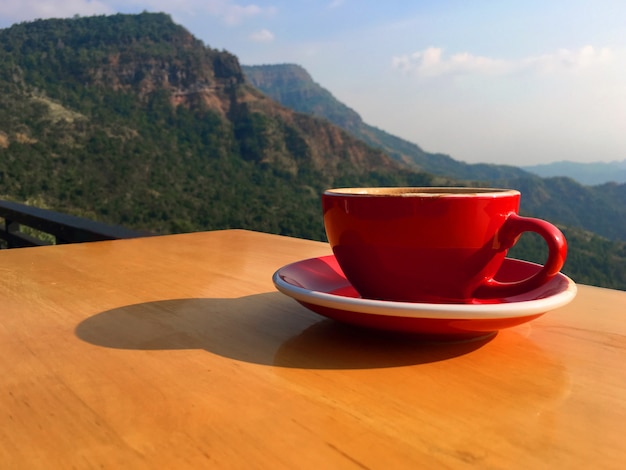 Morning hot latte art coffee in a red cup on wooden balcony at the hillside