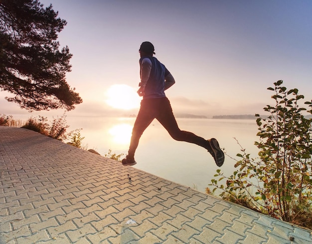 Photo morning jog along river in the park guy runs along the pavement with sun gainst training at dawn