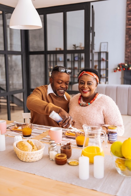 Morning meal. Delighted positive couple smiling while enjoying their tasty breakfast