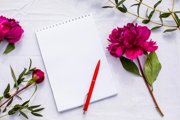 Morning routine for planning or list writing White table surface with binder blank pages and red pen Several flowers placed around to create good mood Everyday planning routine concept