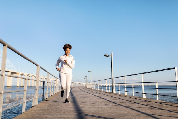 Morning Run Smiling Black Woman In Sportswear Jogging On Pier Near Sea