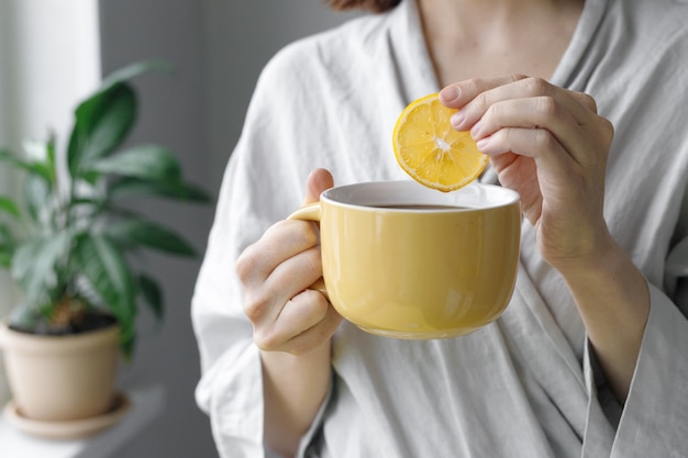 Morning tea with lemon caucasian woman puts lemon in black tea yellow cup