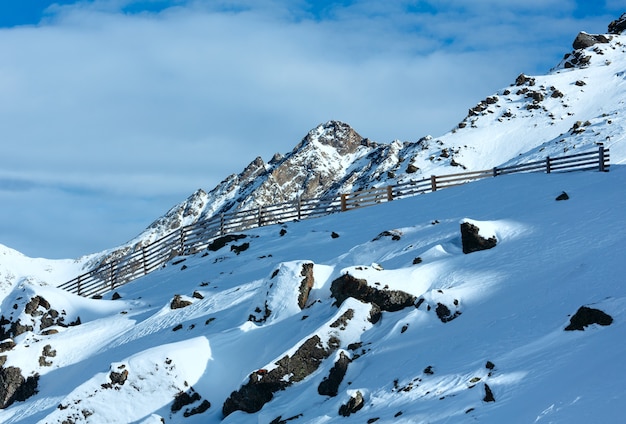 Morning winter mountain landscape with wooden fence along ski track.