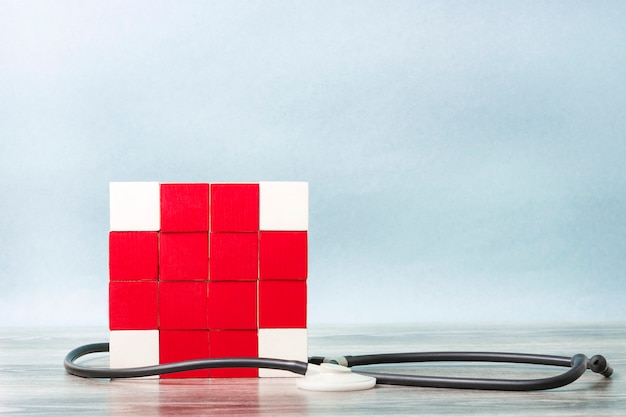 Mosaic of cubes in the form of a red cross entwined with a statoscope. concept of medicine, assistance.
