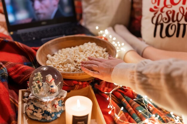 Moscow 11.29.2021. female hand eat popcorn food and enjoyment relaxing watching the movie "home alone" on laptop at home in comfy cozy bed at night on merry christmas or happy new year holidays eve