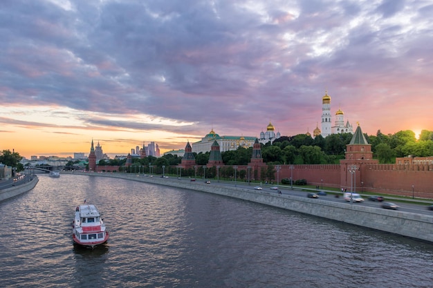 Moscow Kremlin and Moscow River with ships at sunset. Cars traffic on embankment and cloudy sky. Russia.