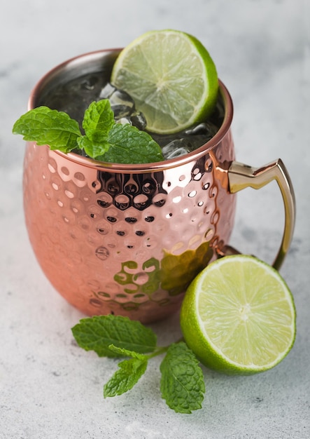 Moscow mule cocktail in a copper mug with lime and mint on light kitchen table background