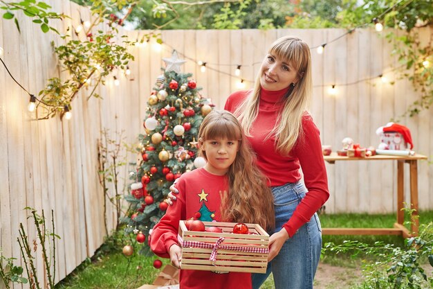 Mother and baby daughter near Christmas tree with gifts, Family Christmas in July. Winter holidays and people concept. Merry Christmas and Happy Holidays Greeting card.