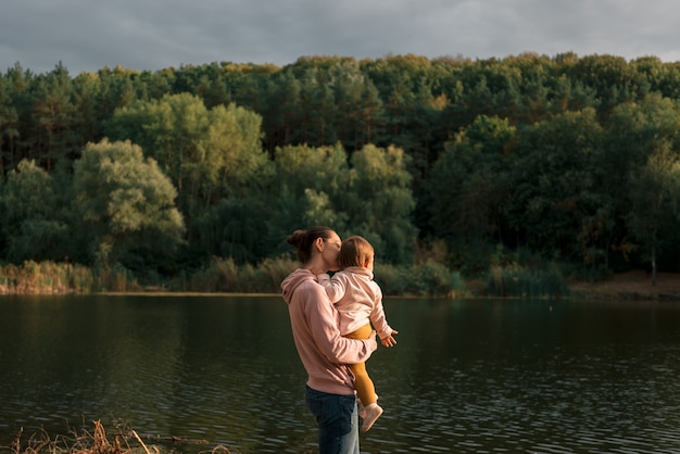 Mother and baby girl sitting near lake. Local travel. New normal vacation. Mother's day