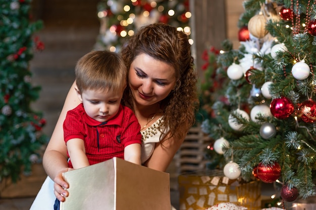 Mother and boy under Christmas tree with gifts. woman with child for new year