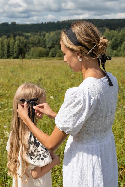 Photo mother braids her daughters hair in the summer on the meadow they are happy