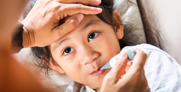 Mother checking temperature of her sick daughter with thermometer in mouth