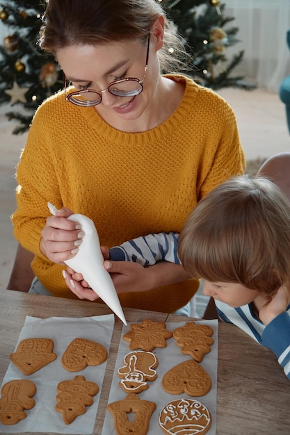 Mother and child decorating Christmas gingerbread cookies with sugar icing and having fun together