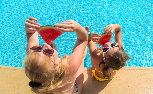 Mother and child eat watermelon by the pool