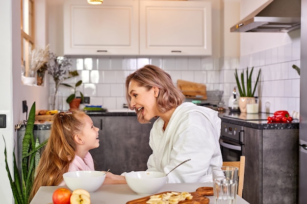 Mother and child girl have fun in the kitchen while having meal, breakfast together