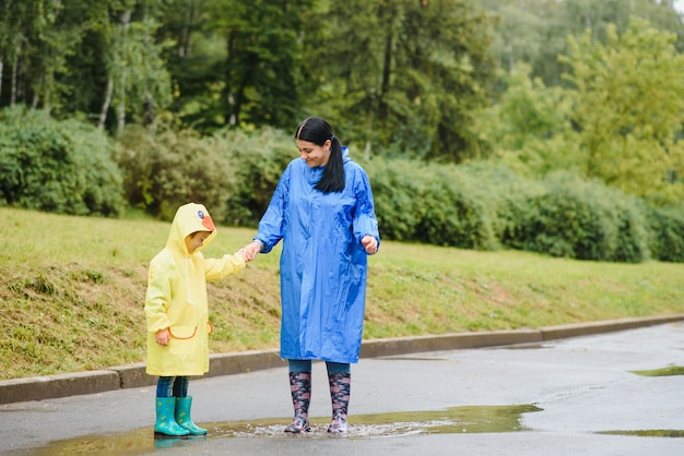 Mother and child playing in the rain, wearing boots and raincoats