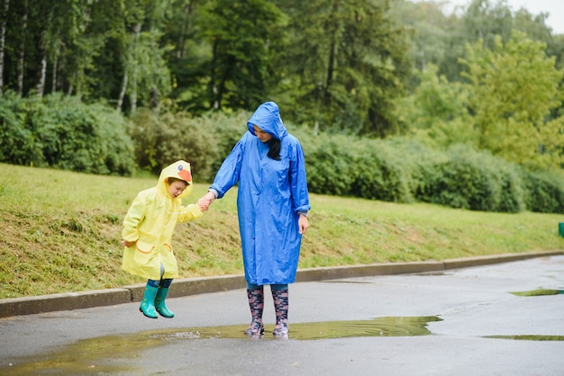 Mother and child playing in the rain, wearing boots and raincoats