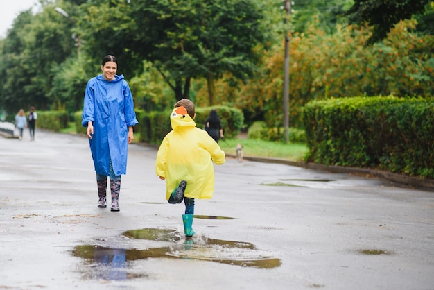 Mother and child playing in the rain, wearing boots and raincoats