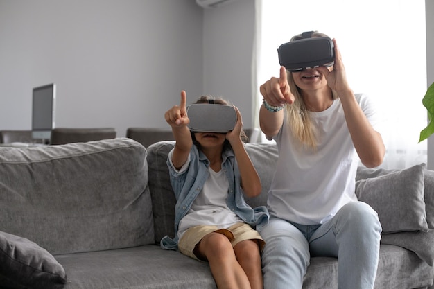 Mother and child wearing virtual reality headset vr glasses in living room at home having fun