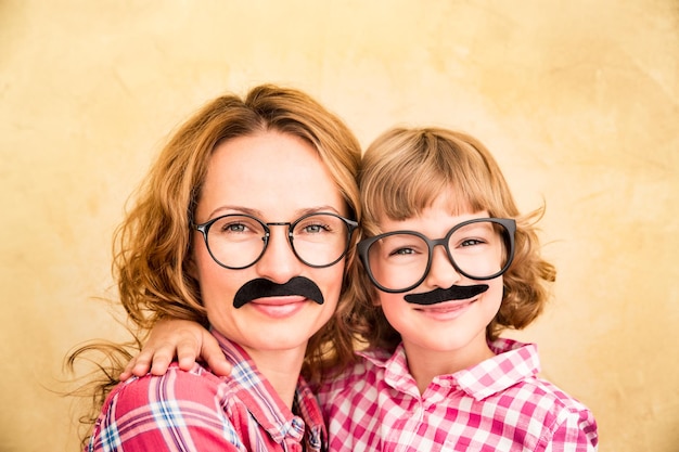 Photo mother and child with fake mustache happy family playing in home