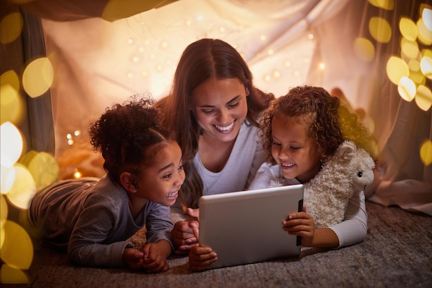 Mother and children live streaming movies on tablet or digital kids app in a tent camping at night and bokeh lights Care love mom reading ebook to happy girl or online games with home wifi in dark