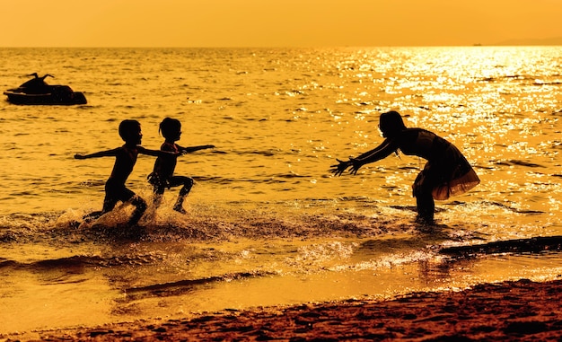 Mother and children playing on the beach at the sunset time. Concept of friendly family.