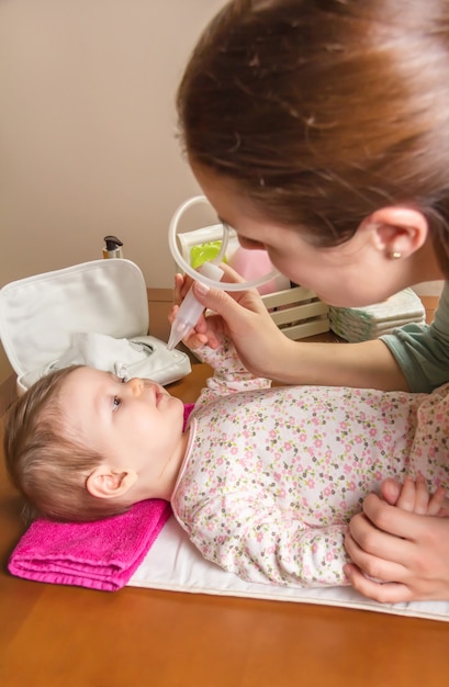 Mother cleaning mucus catarrh of adorable baby with a nasal aspirator