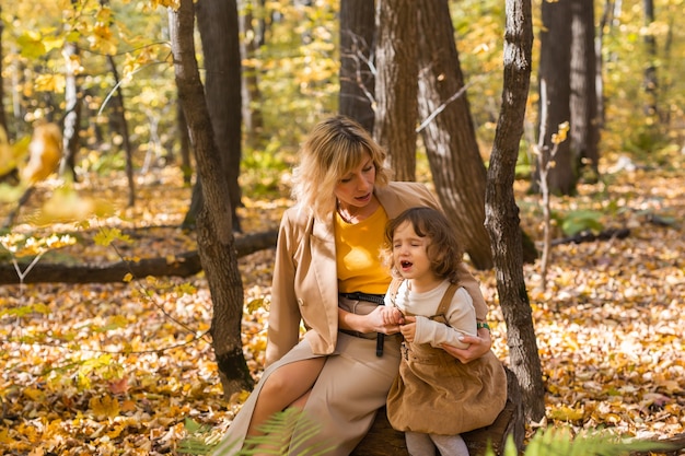 Mother comforting her crying little girl in autumn nature emotions and family concept