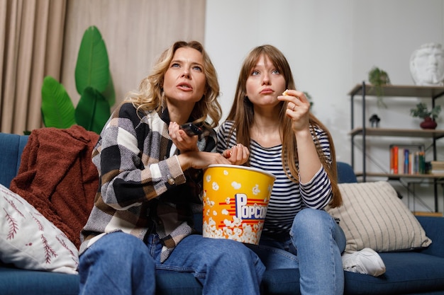 Mother and daughter addicted to watching an interesting movie eat popcorn while sitting on the couch