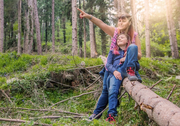 Mother and daughter are doing a selfie sit on the trunk of a tree in the forest