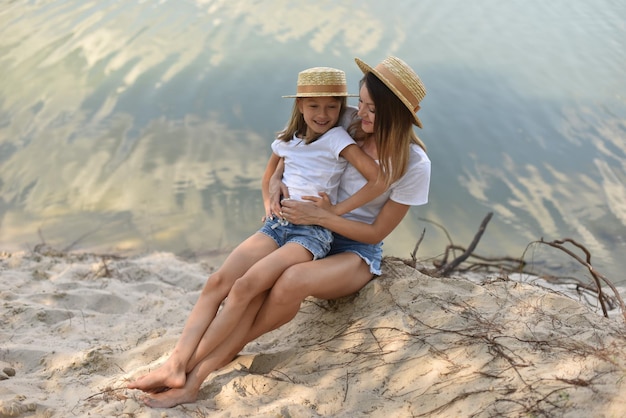 Mother and daughter are sitting on the shore of a lake or river hugging and talking on vacation