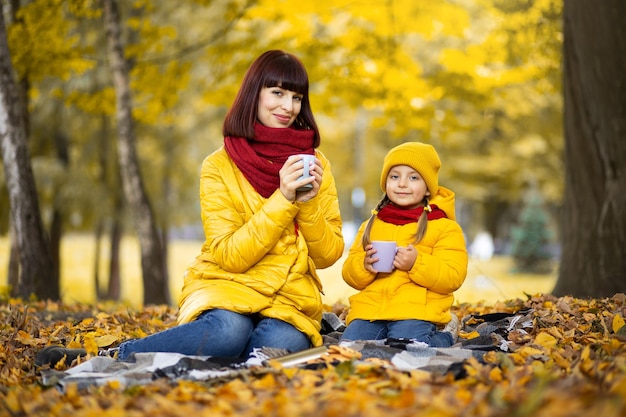 Mother and daughter in autumn yellow park, drinking hot tea