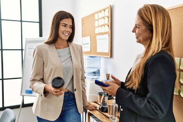 Mother and daughter business workers using smartphone and drinking coffee at office