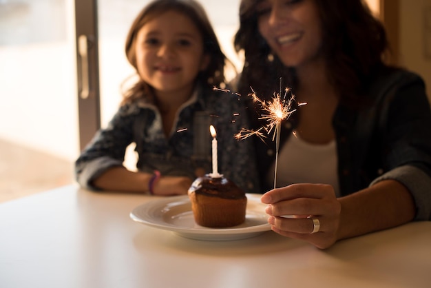 Mother and daughter celebrating birthday with cupcake and sparklers