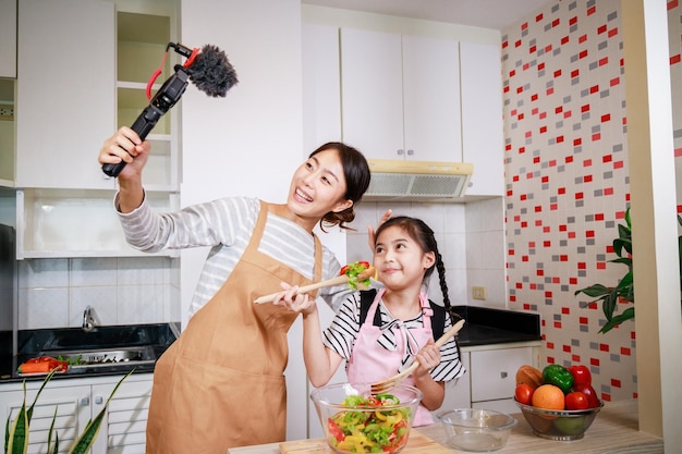 Mother and daughter cooking salad in the kitchen With recording making video blogger together