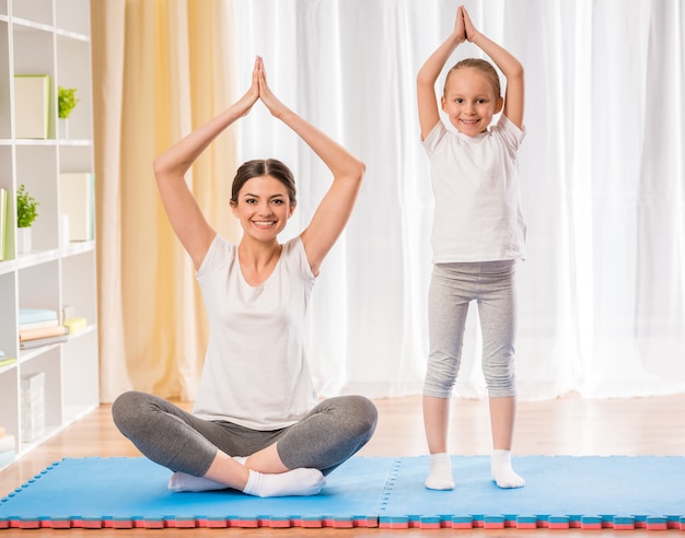 Mother and daughter doing yoga exercises on rug at home.