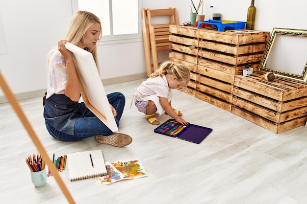 Mother and daughter drawing on canvas sitting on floor at art studio