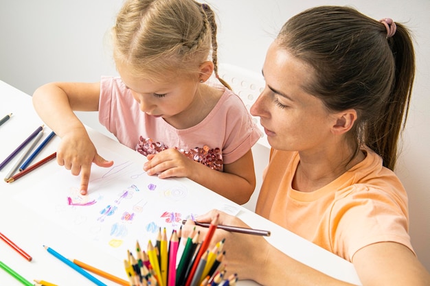 Mother and daughter drawing together with colored pencils on paper Top view flat lay