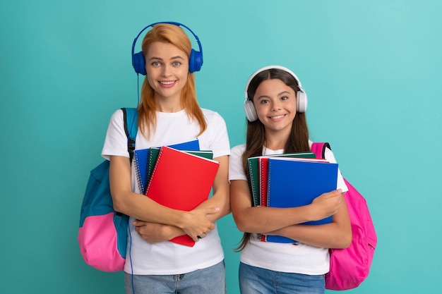 Mother and daughter in earphones hold notebook and backpack ready to study ebook