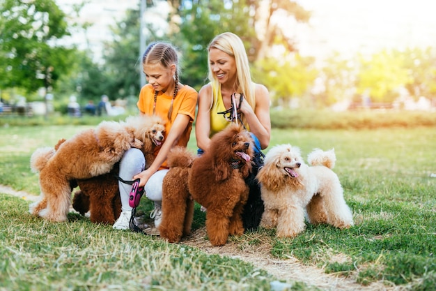 Mother and daughter enjoying together with their poodles in park.