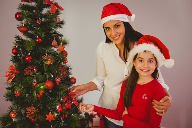 Mother and daughter hanging christmas decorations on tree